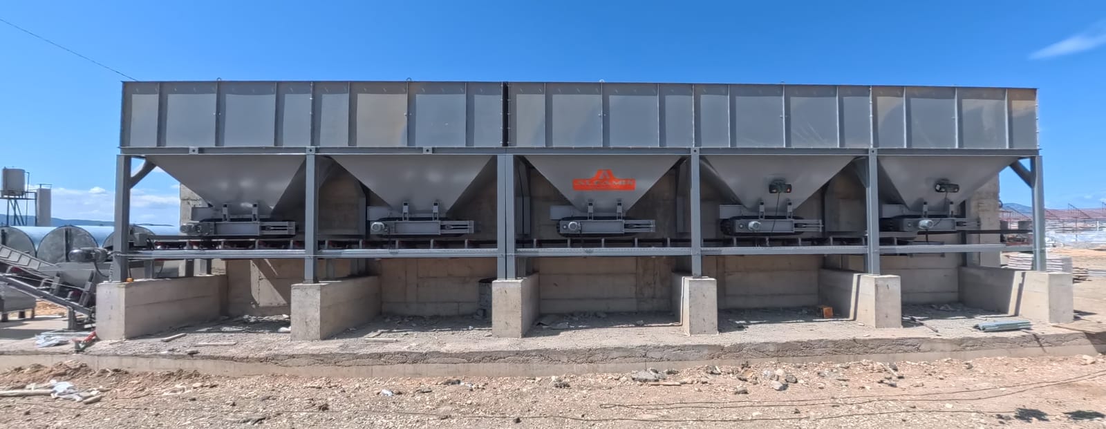 Unité de trémies à granulats d’une centrale d’enrobage : cinq trémies sur appuis en béton et leurs tapis doseurs