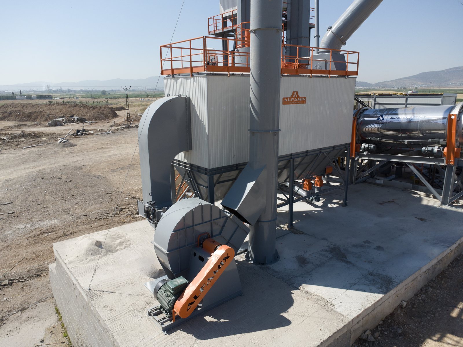 Filtre à manches d’une centrale d’enrobage : caisson du filtre, ventilateur d’extraction et cheminée devant, tambour sécheur à côté
