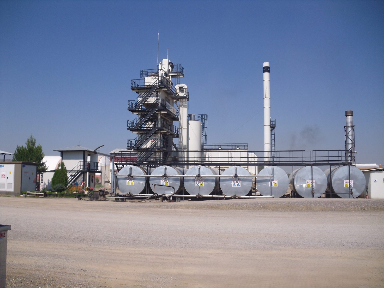 Insulated horizontal bitumen storage tanks lined up in front of an asphalt plant tower